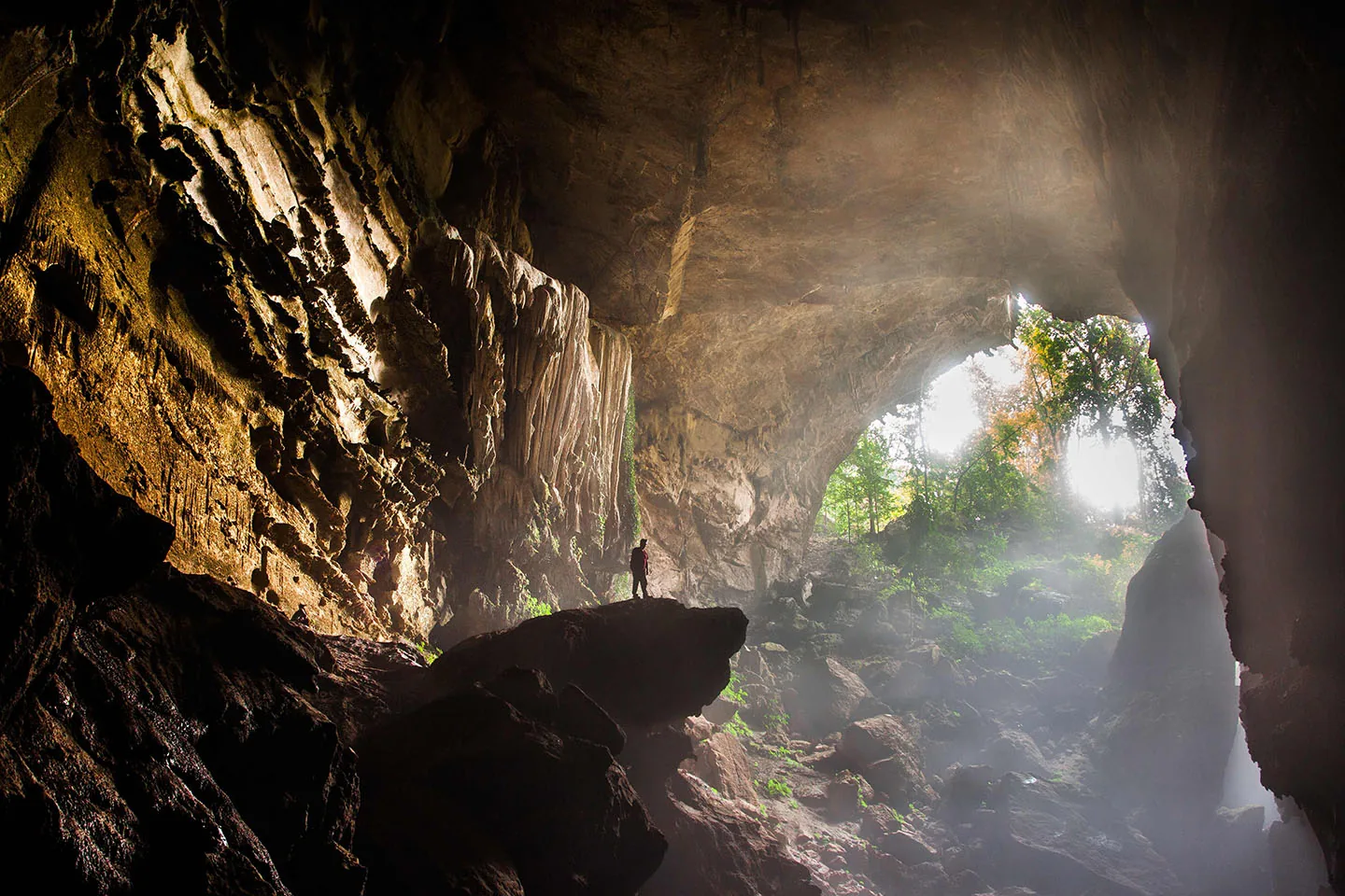 Caver dwarfed by a huge cave entrance in northern Thailand